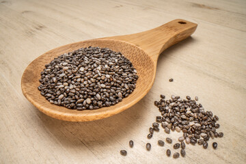 black chia seeds on a wooden spoon against wood table, macro shot