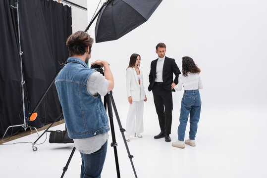 photographer adjusting digital camera while art director talking with models in photo studio.