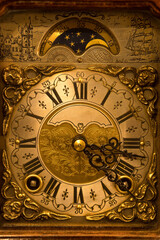 Fototapeta na wymiar Closeup of the dial of an old wind-up table clock made in The Netherlands. Highly decorated vintage wooden clock with moon dial.