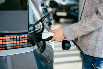 Woman holding charging cable for electric car , looking happy waiting electric car to charge....