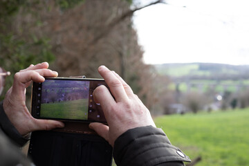Person takes picture of landscape with mobile phone, focus is on screen and hands.
