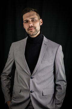 portrait of a young businessman in a gray suit and black turtleneck, looking serious with his hands in his pockets
