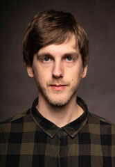 Young handsome tall slim white man with brown hair facing the camera with flannel shirt on grey background