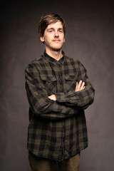 Young handsome tall slim white man with brown hair looking proud with flannel shirt on grey background
