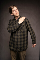 Young handsome tall slim white man with brown hair getting dust off his shoulder with flannel shirt on grey background