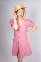 Woman with blonde hair and white skin isolated on grey in pink dress touching her hat by hand