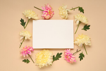 Beautiful chrysanthemums, leaves and blank card on beige background, flat lay. Space for text