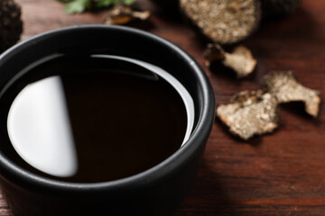 Fresh truffle oil in bowl on wooden table, closeup