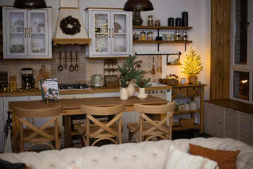 Decorated apartment with festive lights, Christmas tree and gift boxes under in living room, modern dining room with served table