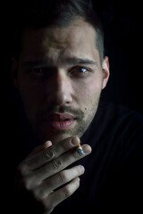 close up portrait of a young man who is smoking holding the last few hits of the cigarette in his hand