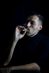 portrait of a young man who is inhaling the smoke of a cigarette while holding it with his hand in his mouth