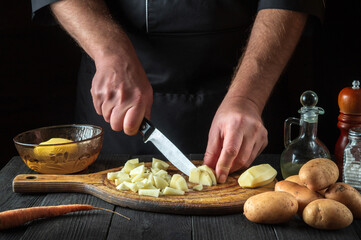 Before making the fries, the chef uses a knife to cut the raw potatoes into small pieces. Close-up of a cook hands while working in a restaurant kitchen