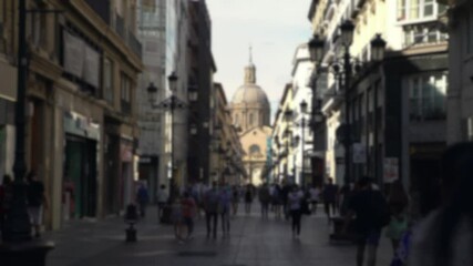 Blurred defocused view of people wear face masks as precautionary measures during coronavirus. Street with the Cathedral Basilica of Zaragoza city. A Roman Catholic church of Spain.