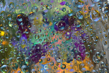 Transparent raindrops falling down against the golden-marsh background with silhouettes of purple-lilac flowers. Abstract fantasy. 