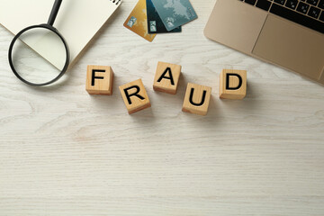 Wooden cubes with word Fraud, credit cards, laptop and magnifying glass on white table, flat lay....