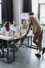 african american businessman standing near cheerful colleagues working at desk in office.