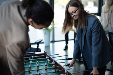 smiling businesswoman playing table football with blurred african american colleague.