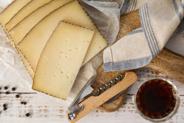 Slices of typical Spanish Manchego cheese and wine on white wooden background