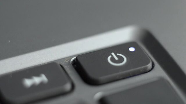 Turning on the laptop. The finger presses the start button on the computer. 