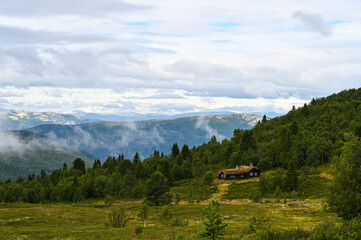 Beautiful landscape in the Rondane National Park in Norway showing a hut surrounded by forest during end of summer. Forested mountains and clouds in the background.