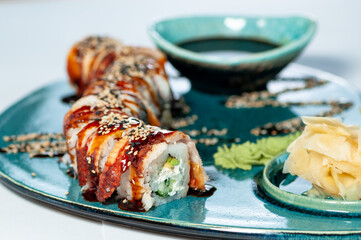dragon sushi roll on a blue curly plate with ginger and soy sauce on a white plate close-up
