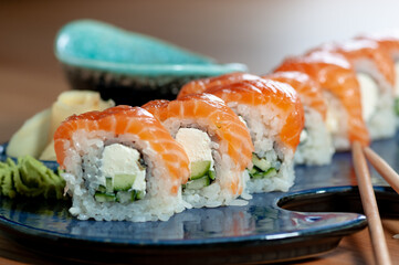 sushi roll philadelphia classic in a blue plate on a wooden table with chopsticks macro photo
