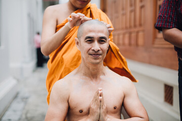 Close-up image of a handsome asian man is shaving hair by head of man who is ordained in Buddhism.