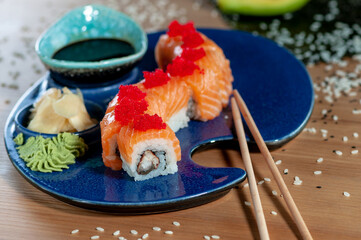 sushi roll dragon philadelphia decorated with red caviar in a blue plate on a wooden table

