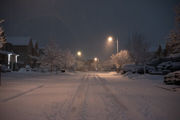Empty street in neighbourhood at night covered in thick blanket of snow with tire tracks in the middle of the street
