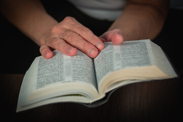 Naklejka premium An older woman (old woman) reads a book, the Bible in transliteration in Russian. An elderly lady and her hands.