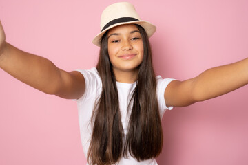 Beautiful girl wearing straw hat standing isolated on pink background feels confident giving a hug to the camera.