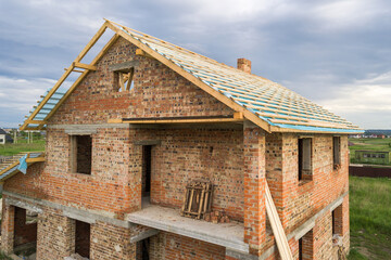Aerial view of a brick house with wooden roof frame under construction.