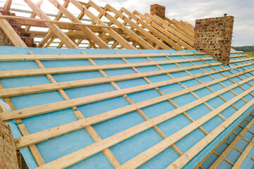 Aerial view of a brick house with wooden roof frame under construction.