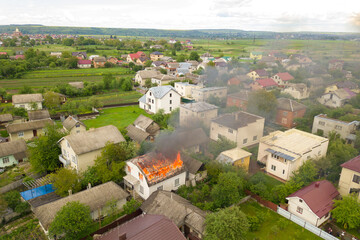Aerial view of a house on fire with orange flames and white thick smoke.