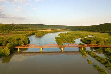 Fototapeta na wymiar Aerial view of a narrow road bridge stretching over muddy wide river in green rural area.