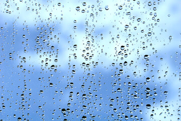 Window glass full of raindrops behind which is a cloudy sky
