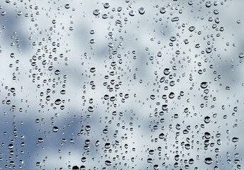 Raindrops on a foggy window behind which is a cloudy sky