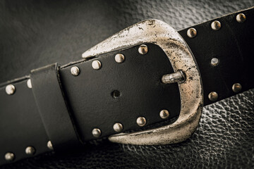 Old leather belt with metal buckle and rivets on dark background
