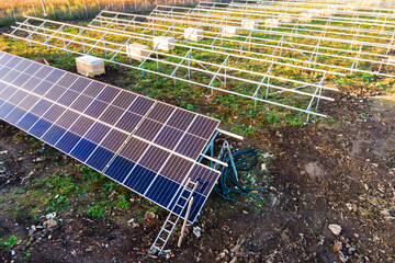 Aerial view of solar power plant under construction on green field. Assembling of electric panels...
