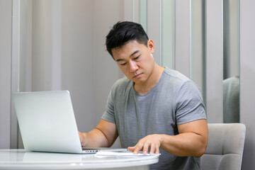 Fototapeta premium of a young man using a laptop computer and looking at documents at his work desk in a comfortable living room