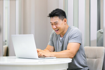Smiling young freelance man using laptop studying online work from home, happy young man typing on laptop pc surfing internet looking at screen enjoying remote work sitting at table