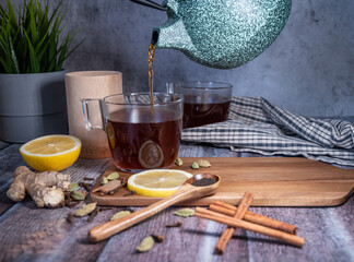 Healthy tea poured into transparent cup. Teapot, lemon, ginger, cardamom, heather bunch and glass jar