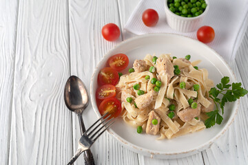 Homemade pasta with green peas, chicken and cream sauce on a white wooden background on a white wooden background