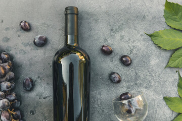Bottle of red wine, green vine, wineglass and ripe grape on vintage dark stone table background....