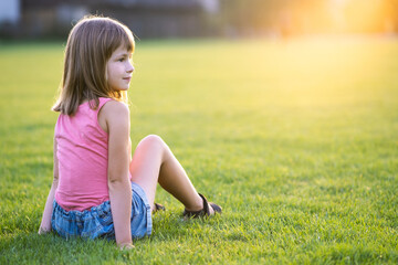 Naklejka na ściany i meble Young happy child girl resting while sitting on green grass lawn on warm summer day