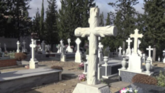 Blurred defocused view of tumbs in a cemetery with headstone, old white cross and cypress tree in Spain. A spanish rural graveyard.