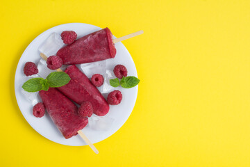 Top view of popsicles with  raspberry on the white plate on the yellow background. Copy space.