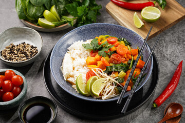 A blue bowl with red thai vegetable curry and basmati rice, fresh lime, cilantro, spinach, chilli...