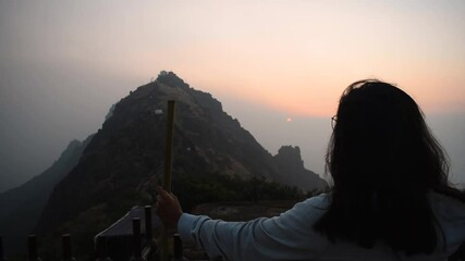 Back view of Indian girl watching sunrise at Girnar Mountain during Cold winter morning. Safe Travel after covid 19 concept. At Girnar hills, Gujarat, India.