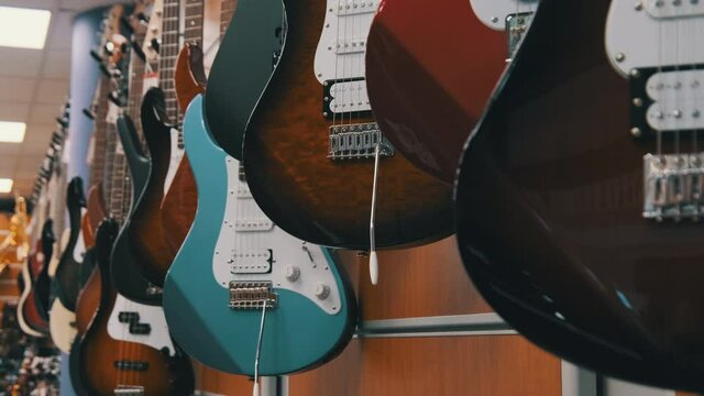 Lot of Multicolored Electric Guitars Hanging in a Music Store, Guitar Shop. Many new different electric guitars are sold in the store. Music instruments shop. A row of Guitars. 4K